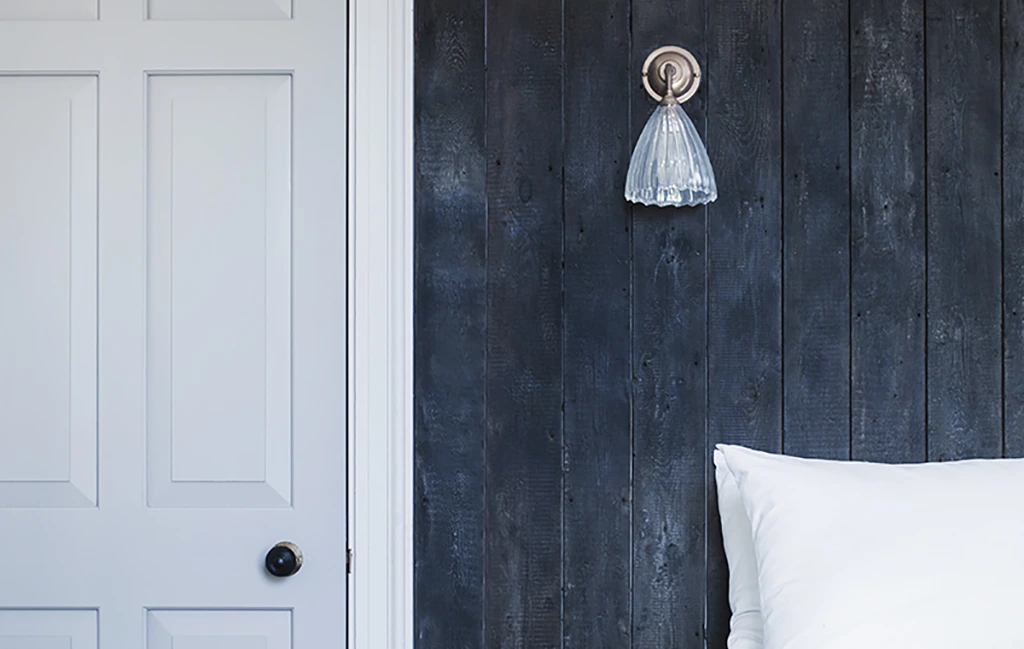 Ribbed Ledbury wall light providing soft bedroom lighting against a dark wood panel wall.