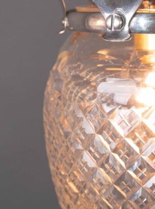 A cut glass pineapple pendant with Arts and crafts silver plated ornate gallery against a dark grey background and photographed up-close to reveal the cut glass details and metal finish.