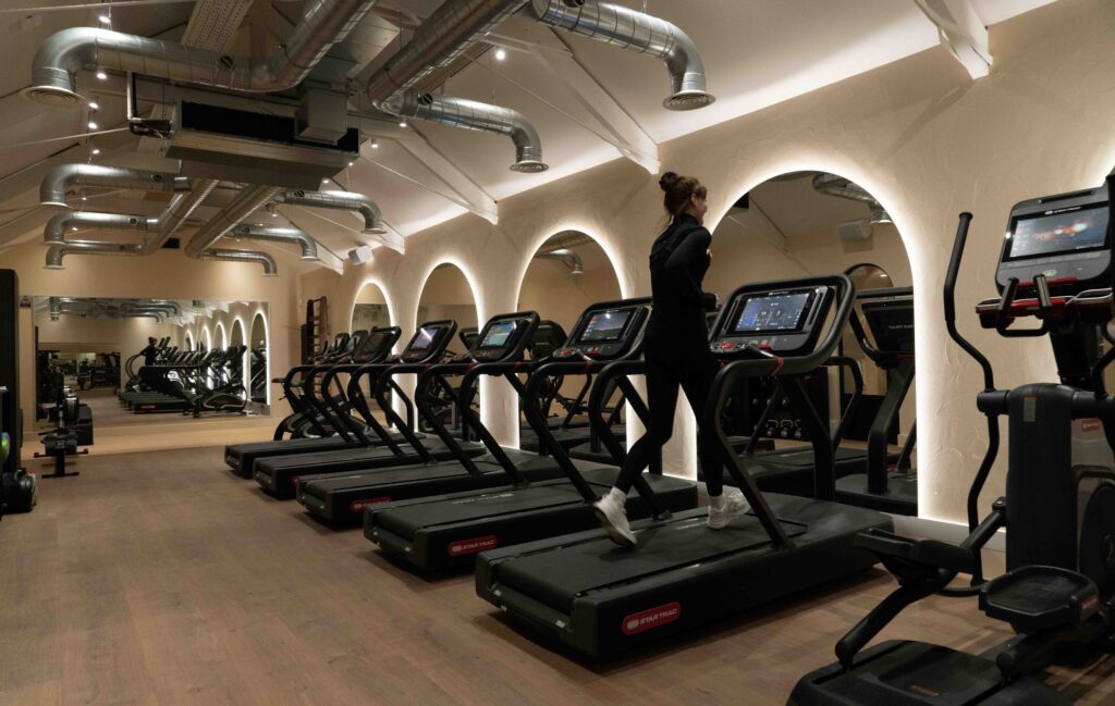 LED strips along large curved mirrors in a large gym, infant of each treadmill.